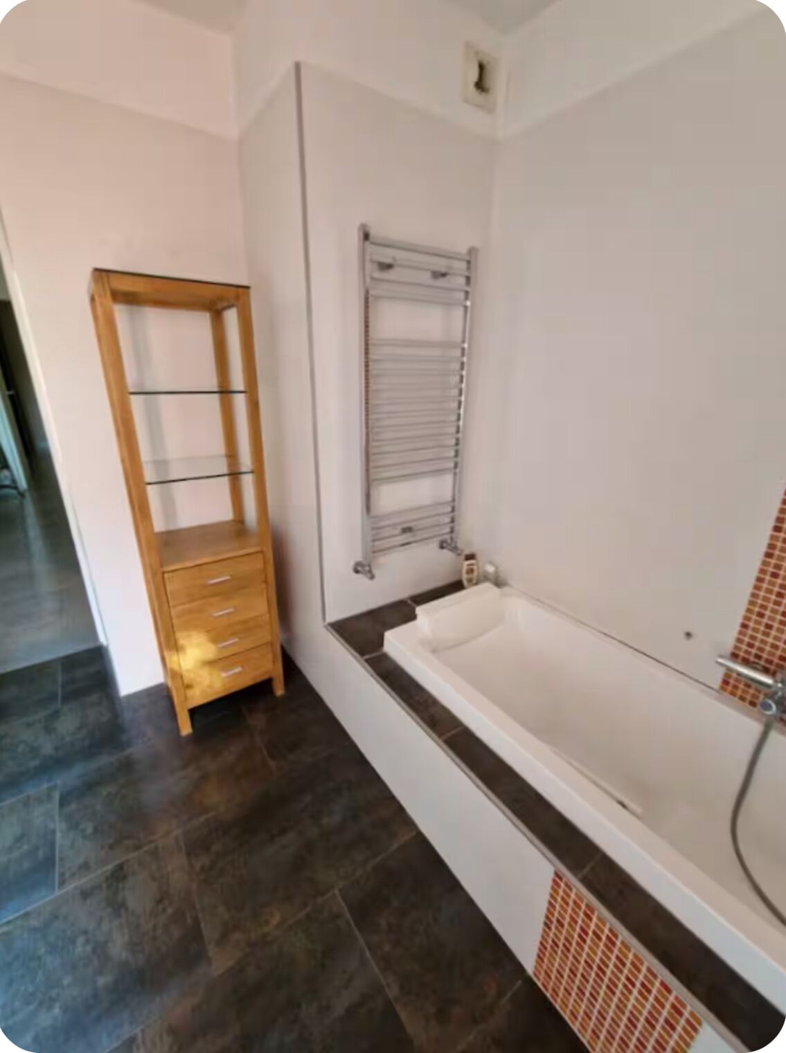 Ein Badezimmer mit einer Badewanne, einer Holzregaleinheit und einem Handtuchhalter.