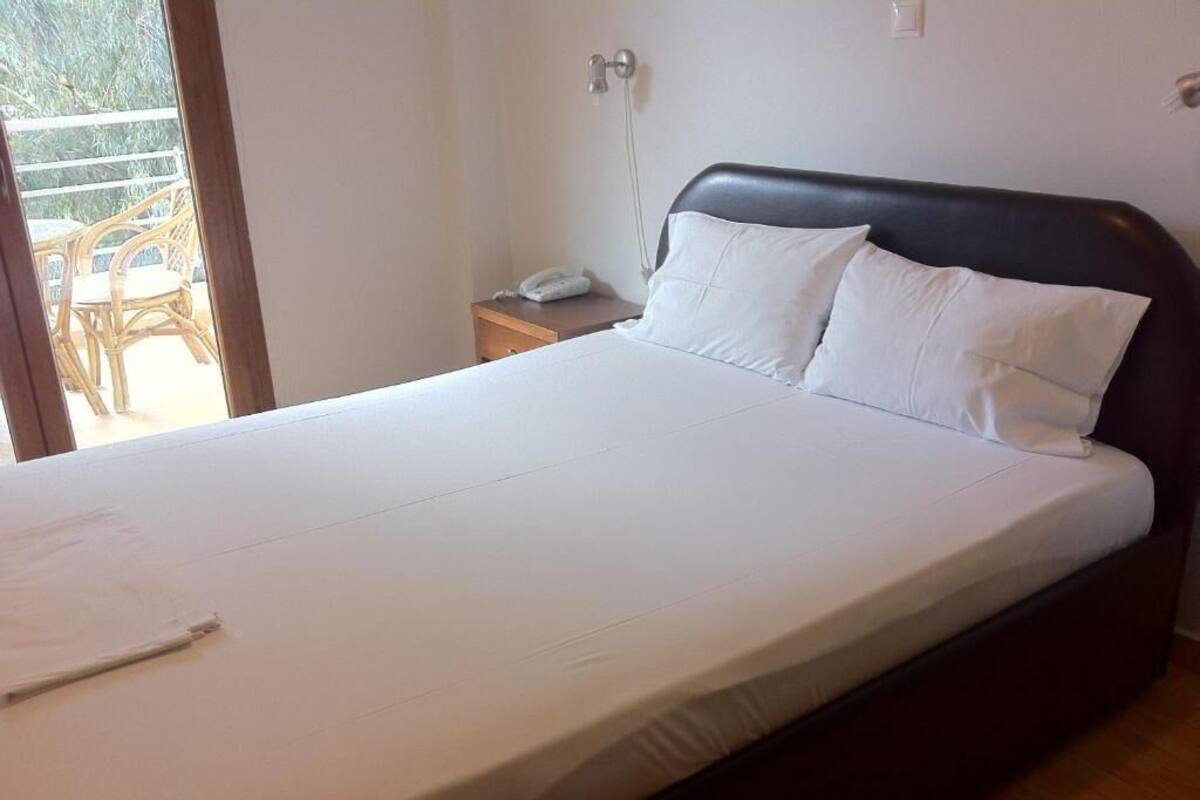 A bed with white linens, a wooden headboard, and a bedside table with a lamp and a phone.