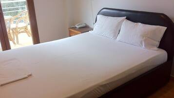 A bed with white linens, a wooden headboard, and a bedside table with a lamp and a phone.
