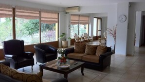 A spacious living room with a sofa set, armchairs, and a coffee table. Large windows with curtains provide ample natural light. - Hotel Magnolia (Istiaia-Aidipsos)
