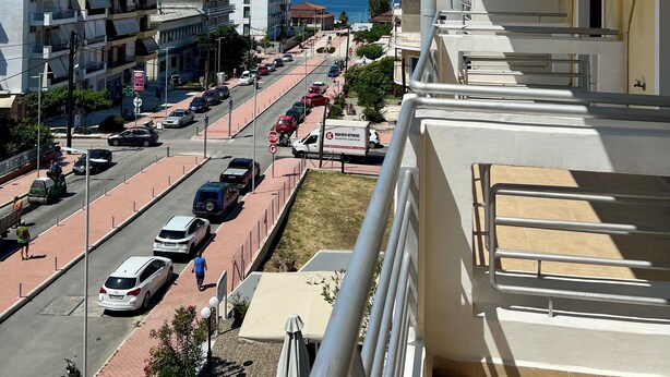 A balcony with a view of a city street, buildings, and a distant mountain range. - Hotel Magnolia (Istiaia-Aidipsos)