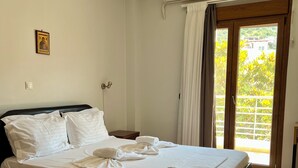 A neatly made bed with white linens and towels, a wooden headboard, a small bedside table, and a wall-mounted air conditioner. - Hotel Magnolia (Istiaia-Aidipsos)