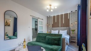 A modern hotel room with a green sofa, a bed with white linens, a marble coffee table, and a laptop. - Shoreditch Luxe (London)