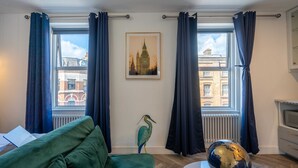A room with a green sofa, a globe on a table, a bird sculpture, and a framed picture of a building. - Shoreditch Luxe (London)