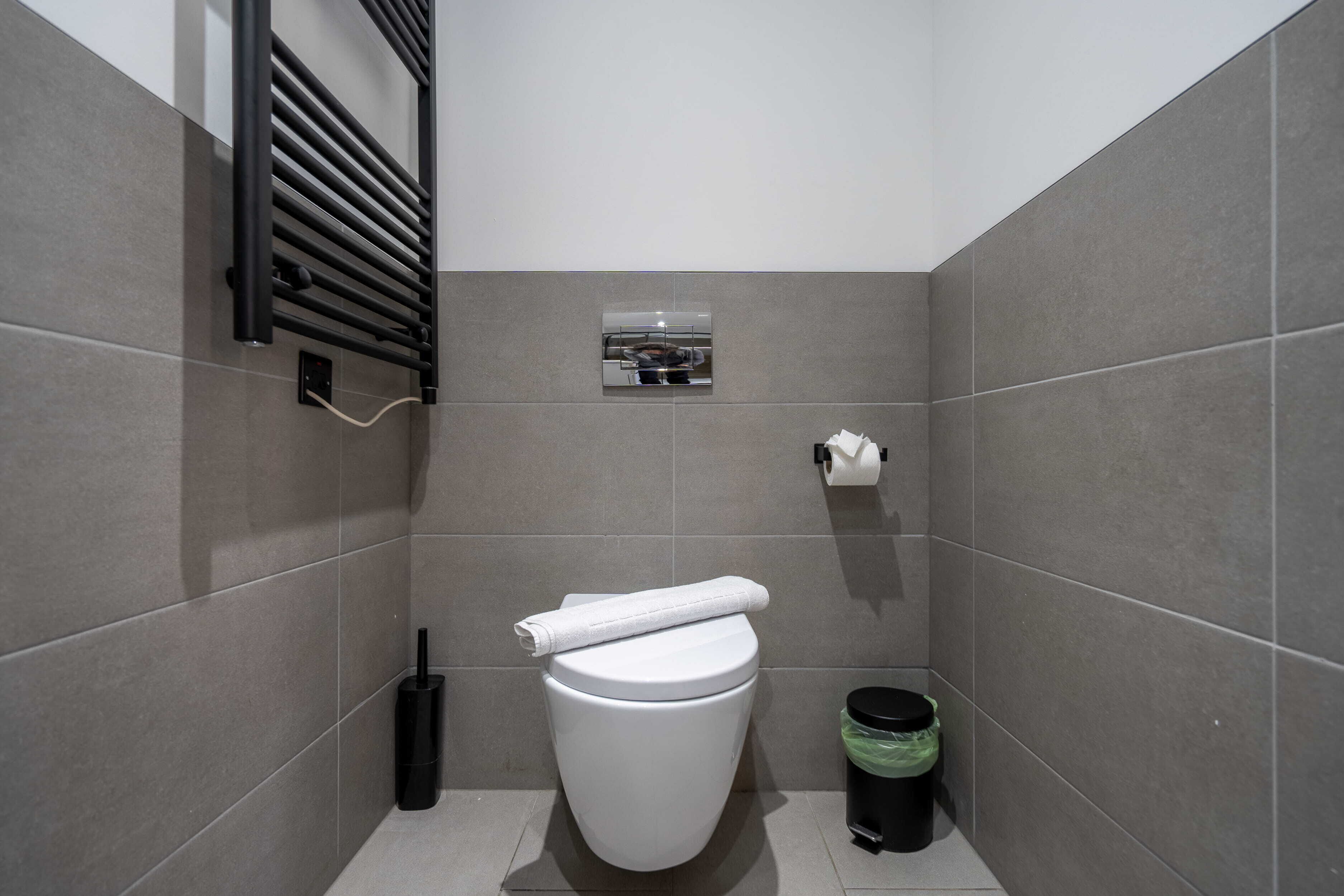 Un baño moderno con inodoro, secamanos, cubo de basura y toallero.