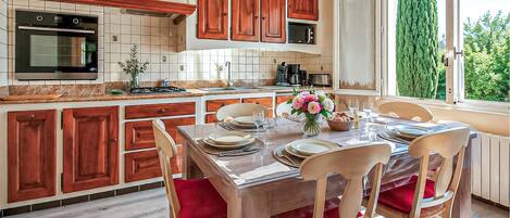 A kitchen with wooden cabinets, a dining table set for four, and a view of greenery outside.