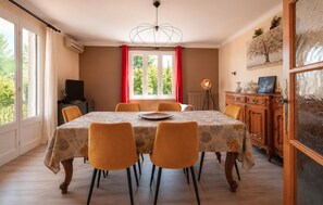 A dining room with a table set for six, a television, and a window with curtains.