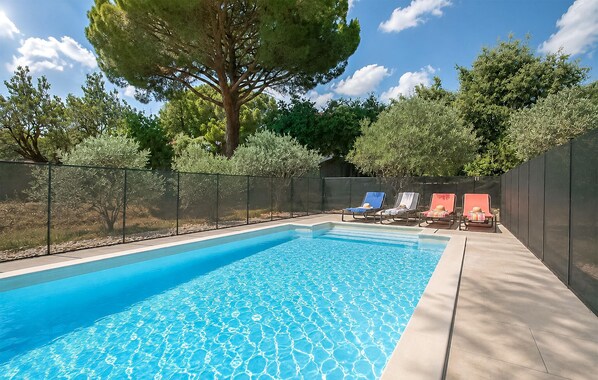 Une piscine à l’eau d’un bleu cristallin, entourée d’une clôture, et trois chaises longues avec des serviettes.