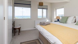 A bedroom with a bed, two windows with views, a radiator, a lamp, and a small stool. - Historic Railway Home - Selsey Seafront (Chichester)