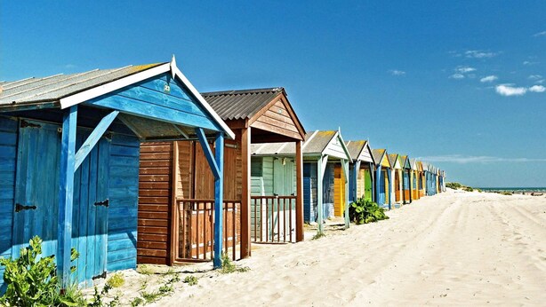 A row of beach huts with a sandy path leading to the beach. - Historic Railway Home - Selsey Seafront (Chichester)