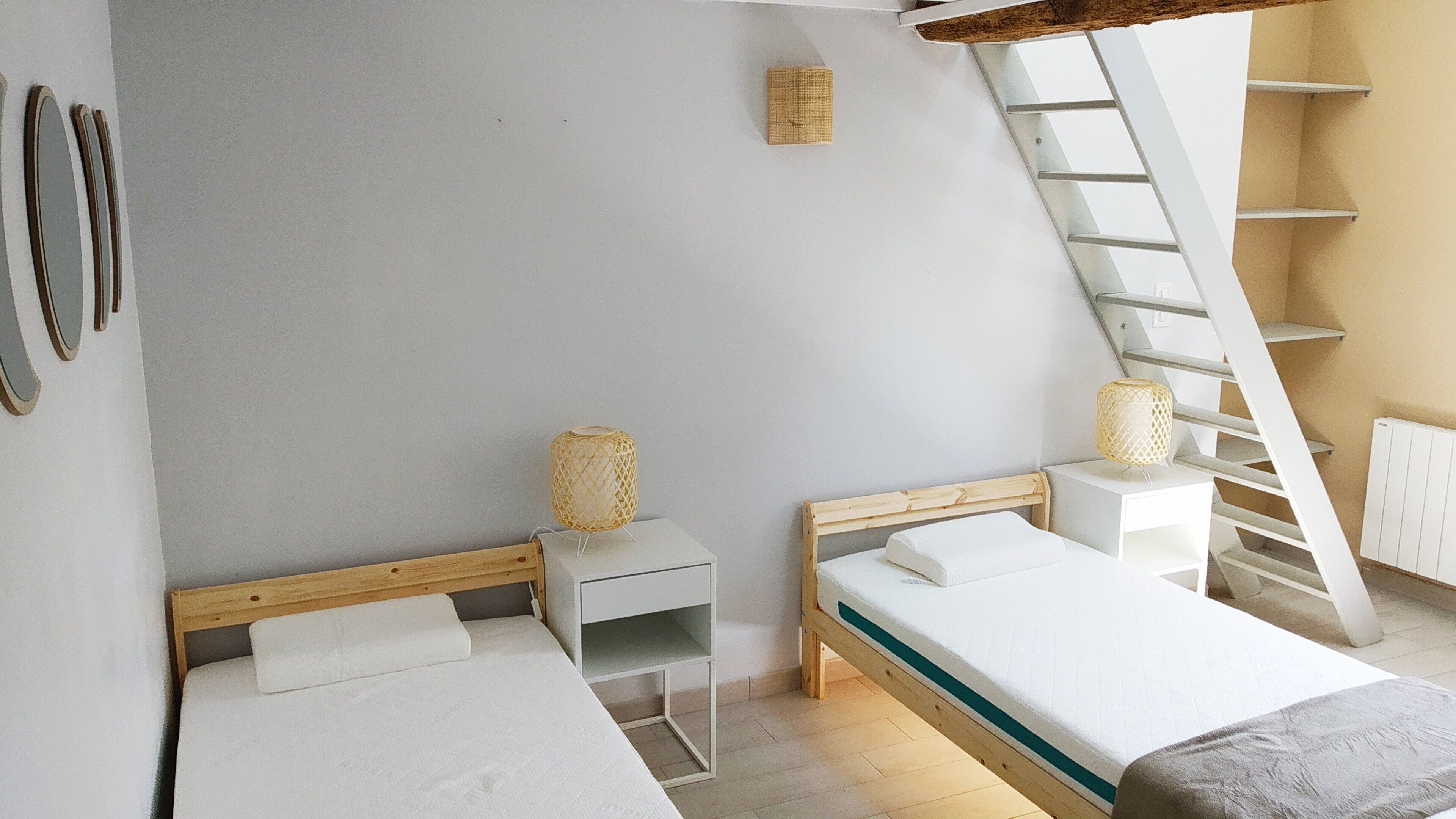 Ein Schlafzimmer mit zwei Betten, einer Wendeltreppe, einem kleinen Tisch und einem an der Wand befestigten Regal.