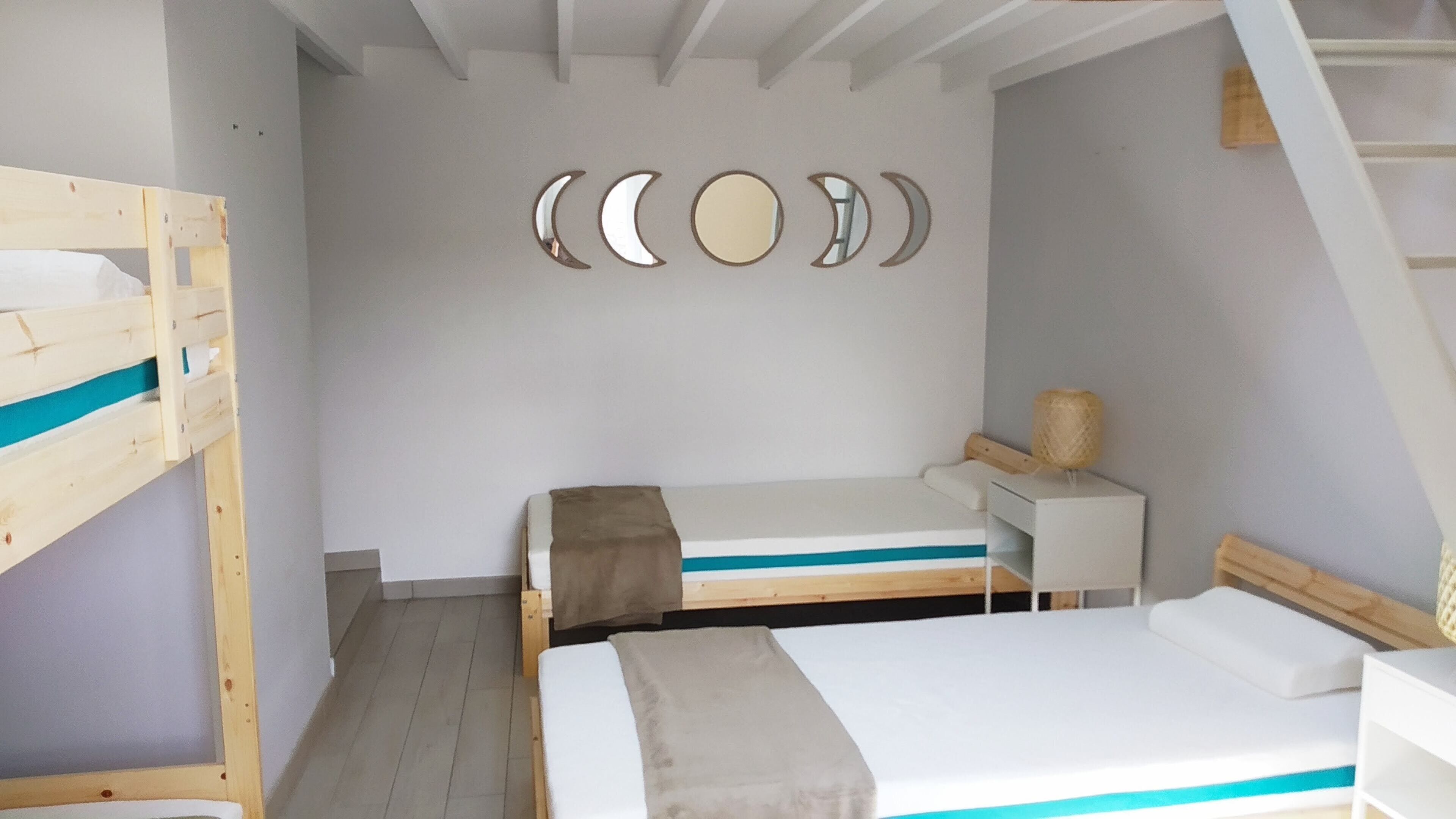 Une chambre avec des lits superposés, un bureau et un mur décoré de motifs représentant les phases de la lune.