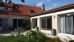 Een huis met een rood pannendak, een stenen gevel en een patio met potplanten en een bloembed in het wit.