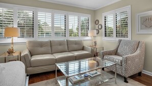 A living room with a beige sofa, patterned armchair, and glass coffee table. - Seagrove Charm + Free Activity Tickets: Bikes, Dolphin Cruise & More! (Santa Rosa Beach)