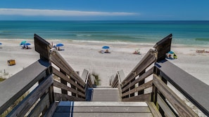 A wooden staircase leading to a beach with umbrellas and beach chairs.