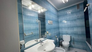 A modern bathroom with blue tiles, a large mirror, a sink, a toilet, and a bidet.