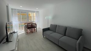 A modern living room with a grey sofa, a dining table with chairs, and a TV on a stand. - TERRASOL MONTERREY 2ªB7 (Torre del Mar)