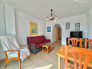 Una sala de estar con sofá, sillón, mesa de centro de madera, televisor y comedor con sillas.