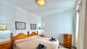 A bedroom with a wooden bed, bedside tables, a dresser, and two wall-mounted lamps. - TERRASOL SAN FRANCISCO 5-2 (Torre del Mar)