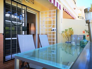 A glass-top table with chairs, a door with a white grid pattern, and a small balcony with a railing and a potted plant. - TERRASOL ALMIJARA 15 (Caleta de velez)