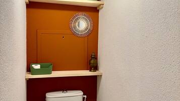 Un bagno compatto con il water bianco, mensole con libri e articoli da toilette, e un elemento decorativo a parete.