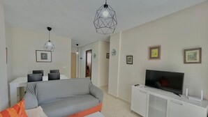 A modern living room with a grey sofa, a white coffee table, a TV on a white cabinet, and two pendant lights. - TERRASOL CAPRI 2 (Torre del Mar)