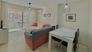 A modern living room with a sofa, dining table, and chairs. There is a window with curtains, a ceiling fan, and framed pictures on the wall. - TERRASOL CAPRI 2 (Torre del Mar)