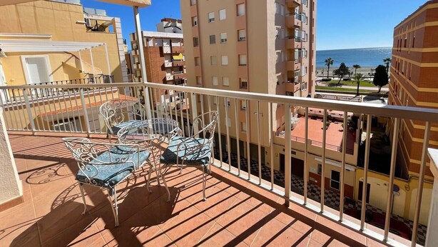 Un balcón con vistas a la costa, que incluye un edificio de varios pisos y balcones.