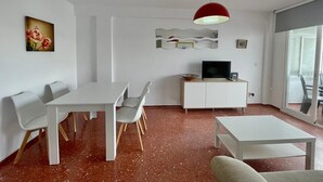 Un saló modern amb zona de menjador, un televisor sobre un moble blanc i un finestral gran.