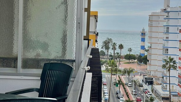 Un balcó amb vista al mar, una cadira i un edifici amb façana blava i blanca.