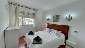 Un dormitori amb un llit, una taula de nit, persianes a la finestra i una làmpada penjant a la paret.