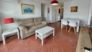 Un saló amb un sofà, una taula de centre, una taula de dinar amb caires, una làmpada penjant vermella i obres d'art a les parets.