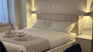 Una cama bien hecha con cabecera, dos lámparas de noche y un juego de toallas sobre la cama.