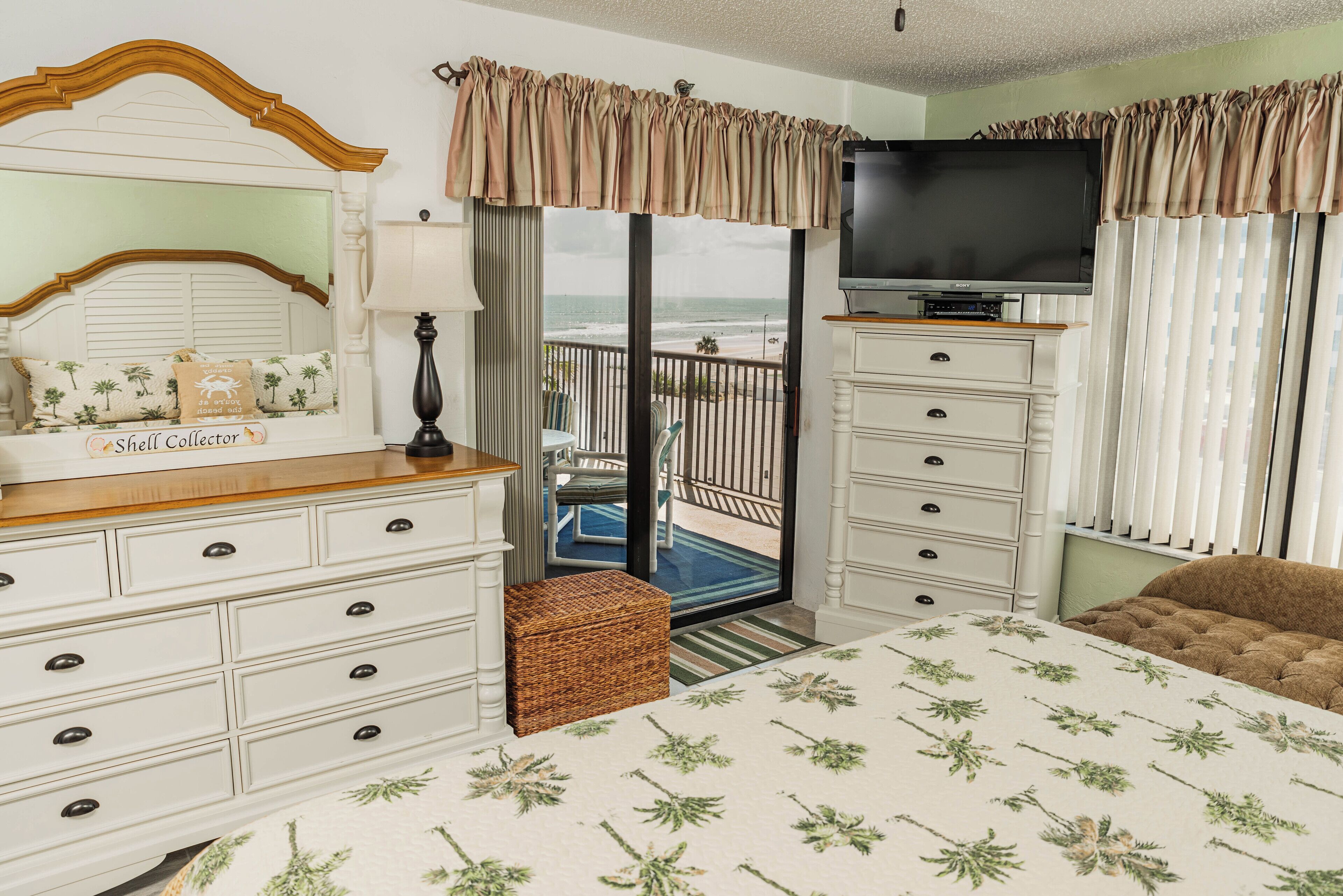 Un dormitorio con cama, cómoda, televisor y vista al océano.