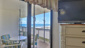 Un balcón con televisor, una mesa de comedor y sillas, con vista a la playa.