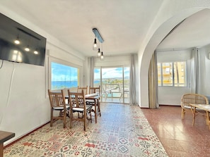 Un coin repas avec vue sur la mer, un téléviseur fixé au mur et un sol à motifs.