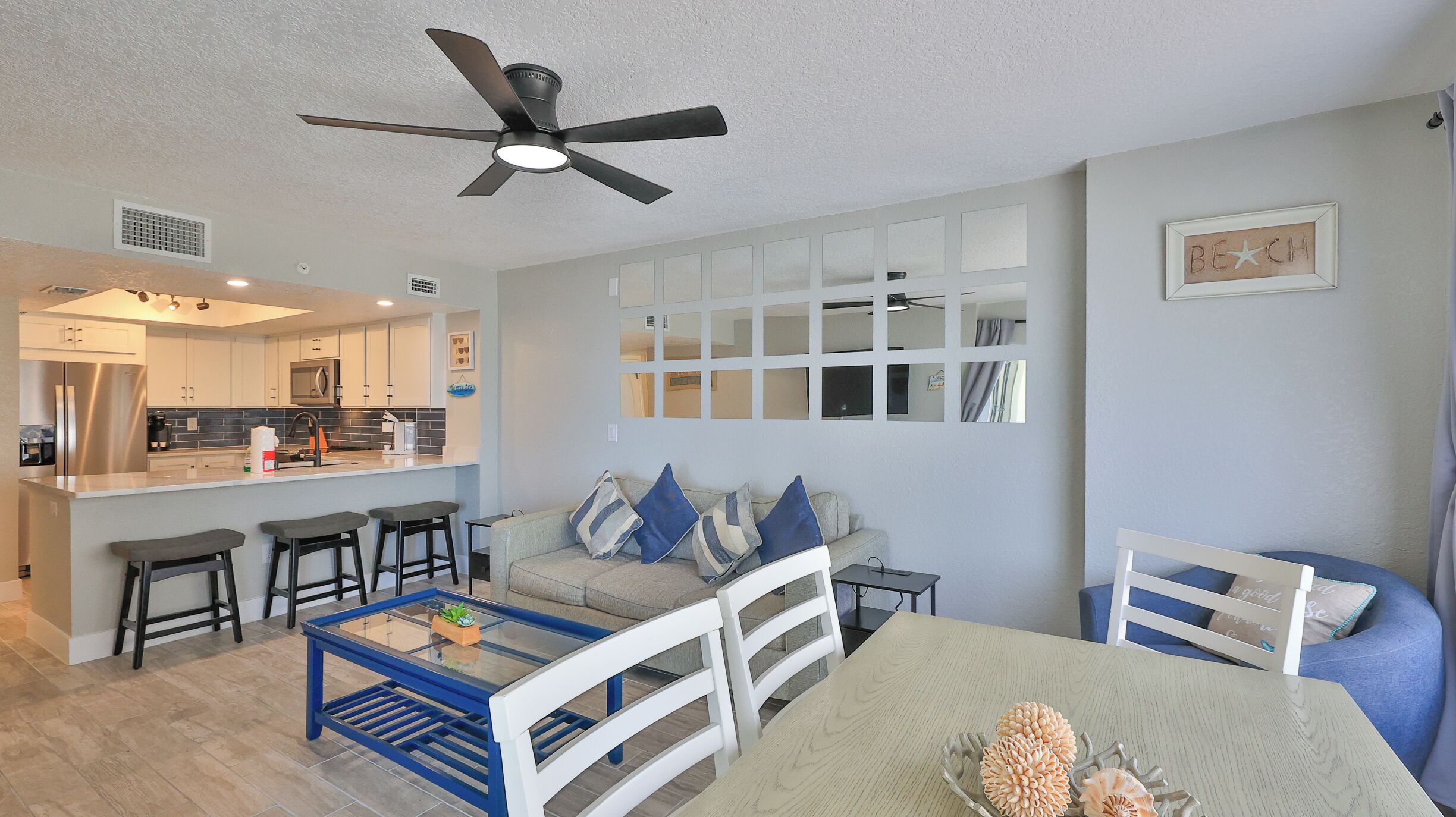 A modern living room with a kitchen, a ceiling fan, and a dining area with a table and chairs.