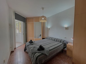Een slaapkamer met een bed, een kledingkast, een spiegel en een hanglamp.