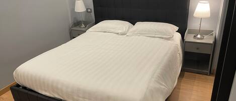 A neatly made bed with a dark headboard, two bedside tables with lamps, and a wooden floor.