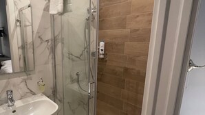 A modern bathroom with a glass-enclosed shower, a marble sink, and wooden flooring.