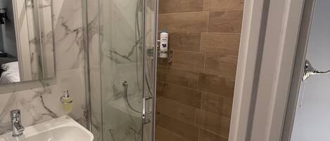 A modern bathroom with a glass-enclosed shower, a marble sink, and wooden flooring.