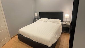 A bedroom with a bed, two bedside tables with lamps, a wooden floor, and a ceiling with recessed lighting.