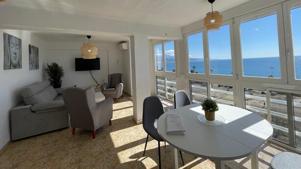Una sala de estar moderna con un sofá, sillas, televisor y una mesa de comedor con vistas al mar.