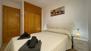 Un dormitorio con cama, mesita de noche con lámpara, un cuadro en la pared y dos armarios de madera.