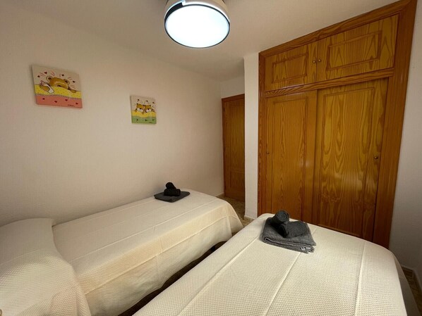 A bedroom with two single beds, a wooden wardrobe, and two wall art pieces. - TERRASOL MIGUELANGELO FRONTAL AL MAR (Torre del Mar)