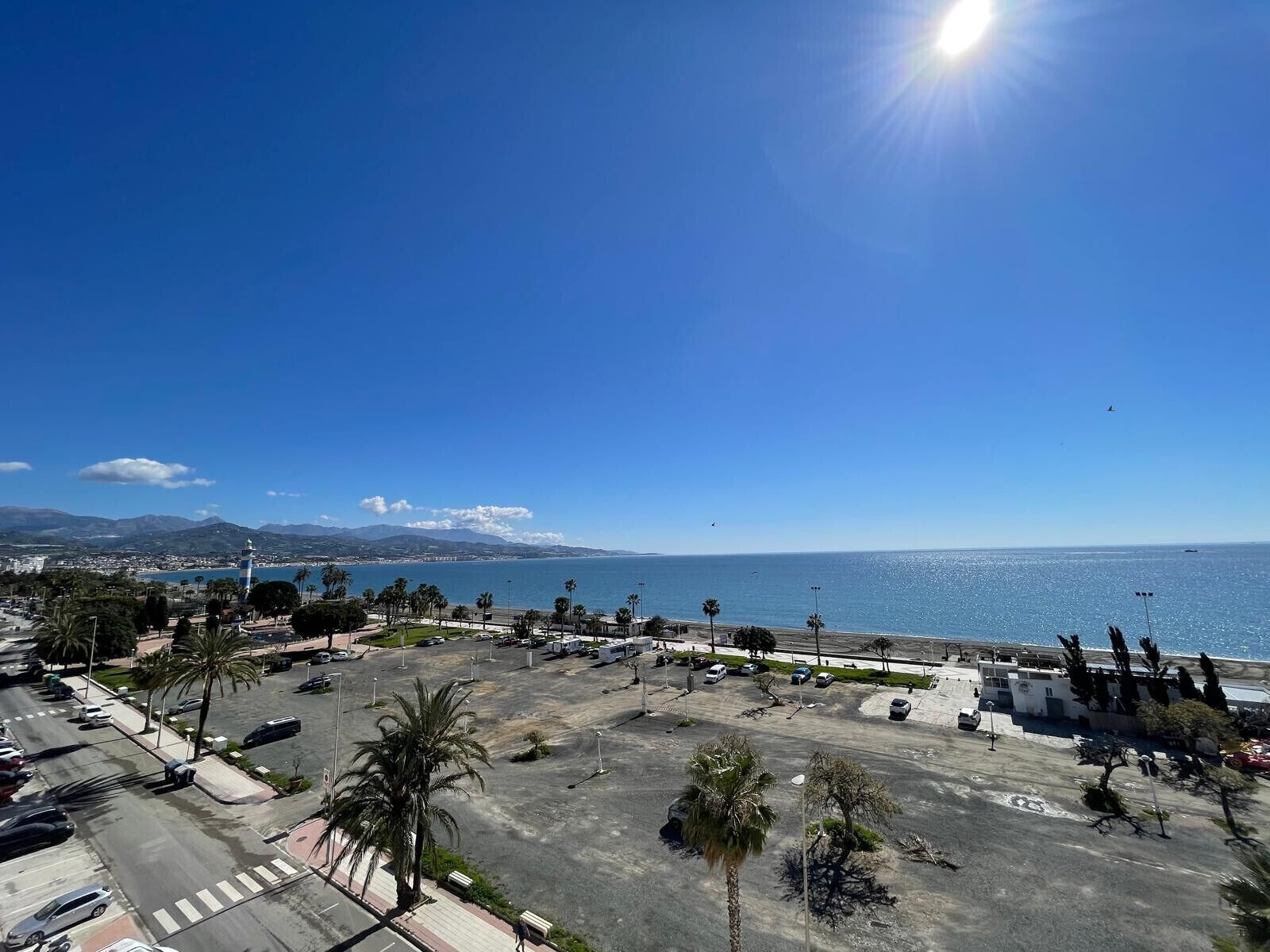 A parking lot with palm trees and a view of the sea.