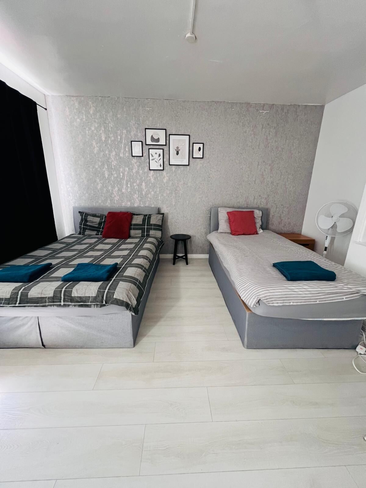 Une chambre moderne avec deux lits, un petit tabouret et un ventilateur fixé au mur.