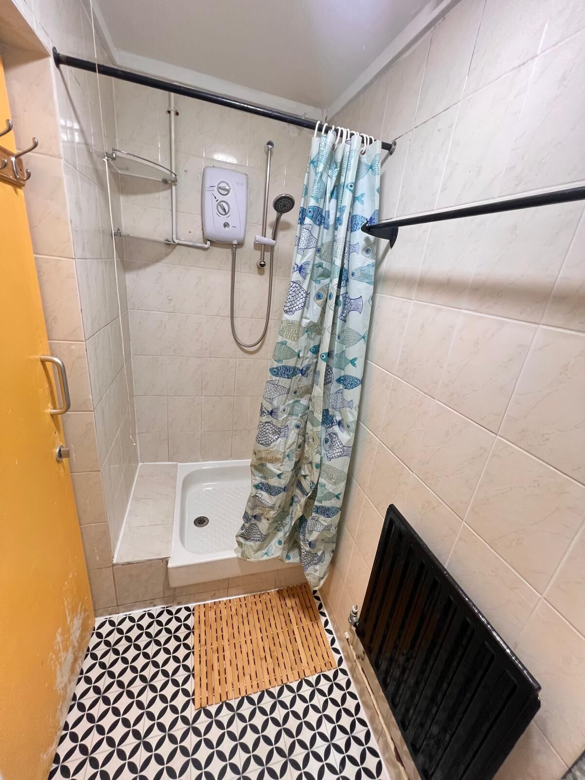 Un espacio de ducha pequeño con cabezal, panel de control y cortina decorada con motivos de peces.