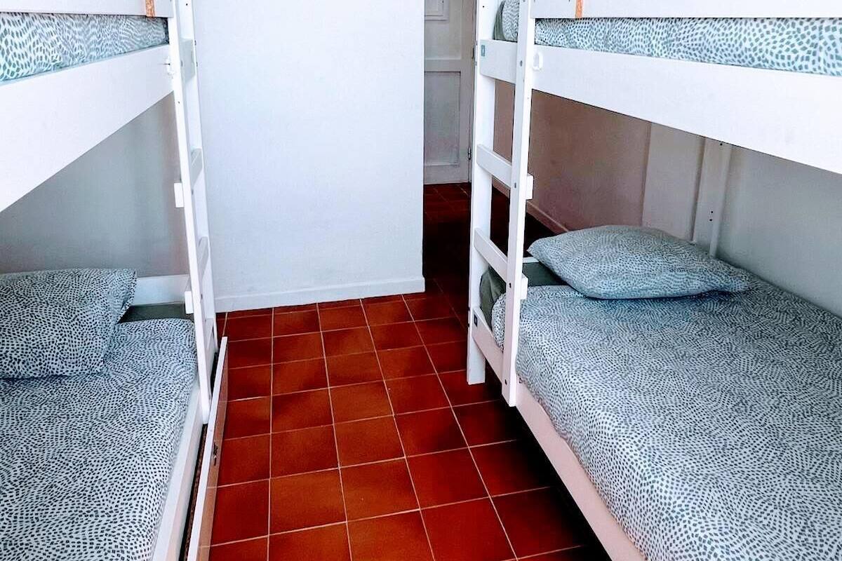 Una habitación con literas, suelo de baldosas y una puerta que da a otra estancia.