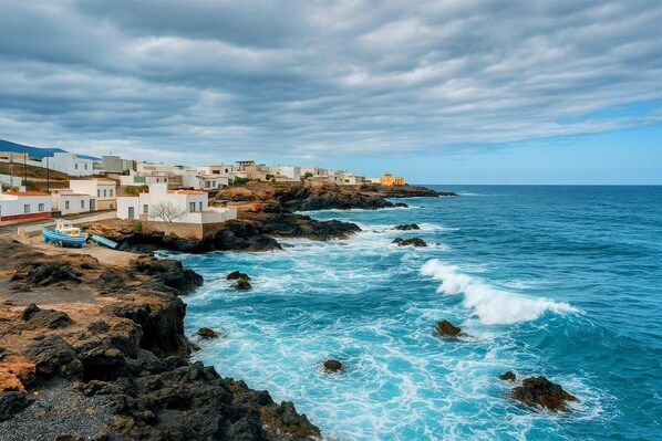 Un pueblo costero con edificios blancos, costa rocosa y un bote.